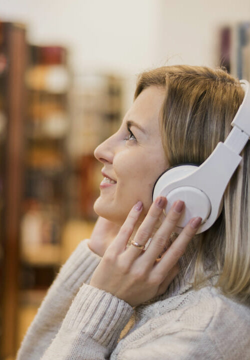 Mulher ouvindo música com fones de ouvido em uma biblioteca, representando o aprendizado de inglês por meio de músicas.