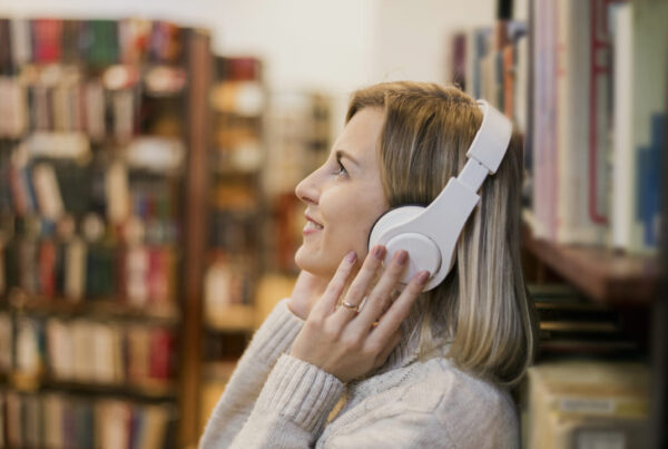 Mulher ouvindo música com fones de ouvido em uma biblioteca, representando o aprendizado de inglês por meio de músicas.
