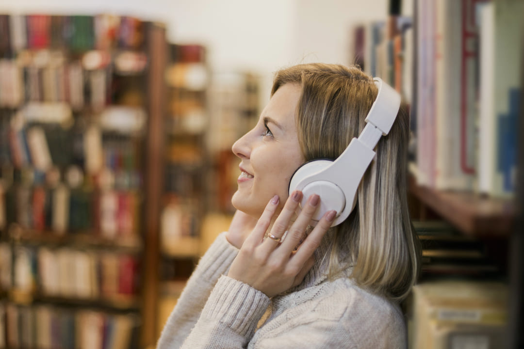 Mulher ouvindo música com fones de ouvido em uma biblioteca, representando o aprendizado de inglês por meio de músicas.