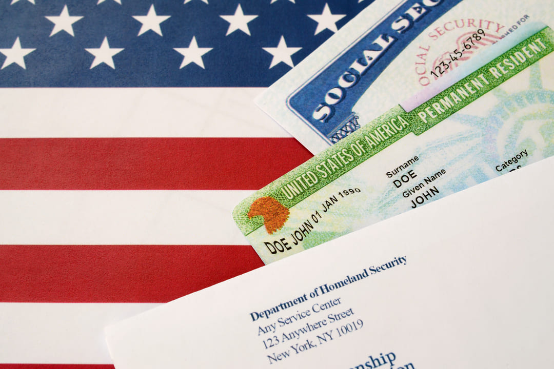 Cartões do Green Card e Social Security sobre uma bandeira dos Estados Unidos, ao lado de uma carta do Departamento de Segurança Interna.